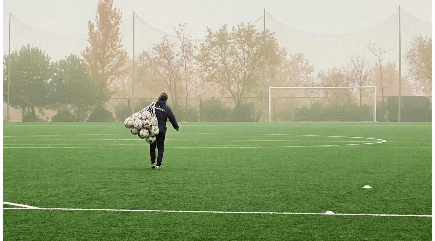 Coach is walking on to soccer field with bag of balls