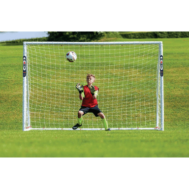 HART Samba Match Goals – goalkeeper in red and black uniform attempting save in front of white soccer goal on green grass field.